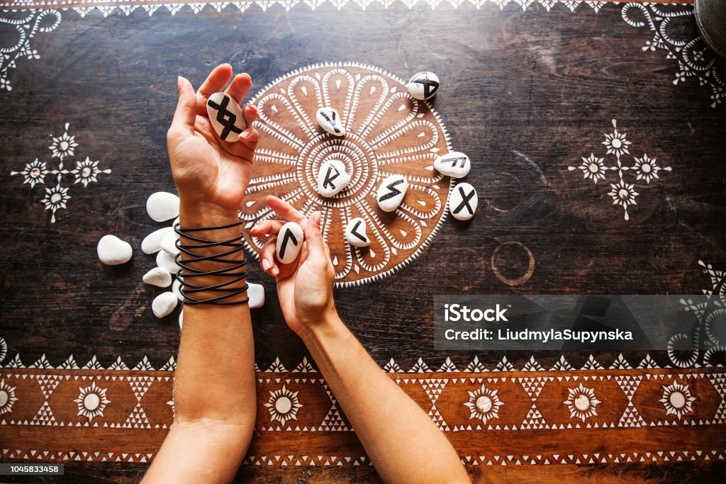 hands holding runes stones on an ornate table