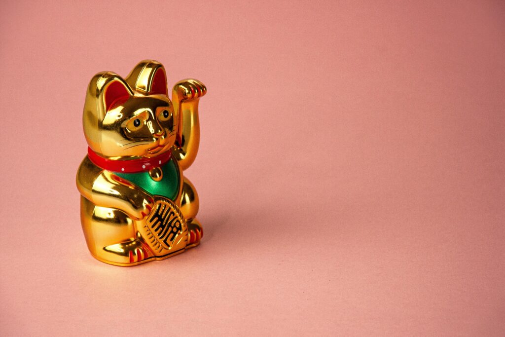 pexels-photo-6441625-6441625 A golden Maneki Neko statue against a pink background, symbolizing luck and prosperity.