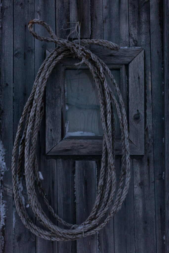 Close-up of a rustic rope hanging on a barn's wooden wall, creating a rural, textured feel.